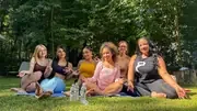 A group seated together on the grass beneath trees.