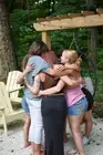 Participants embracing outdoors beside a wooden arbor.
