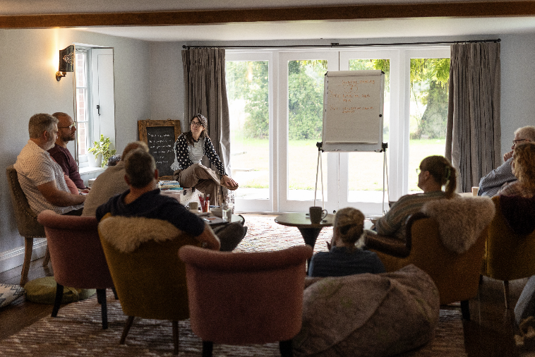 Alice leading a retreat session with the group in armchairs by the garden windows