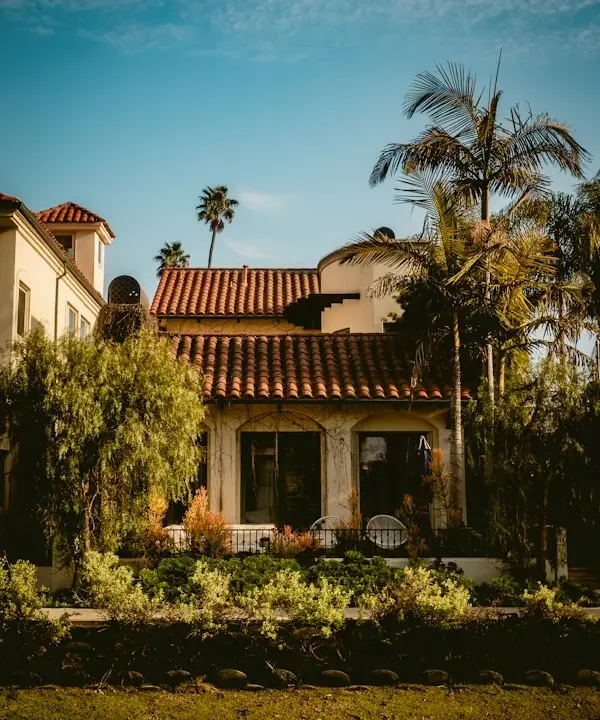 Spanish Revival home with a red tile roof and palms in late-afternoon light