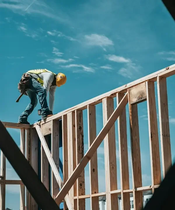 Builder on the wood framing of a new house under a blue sky