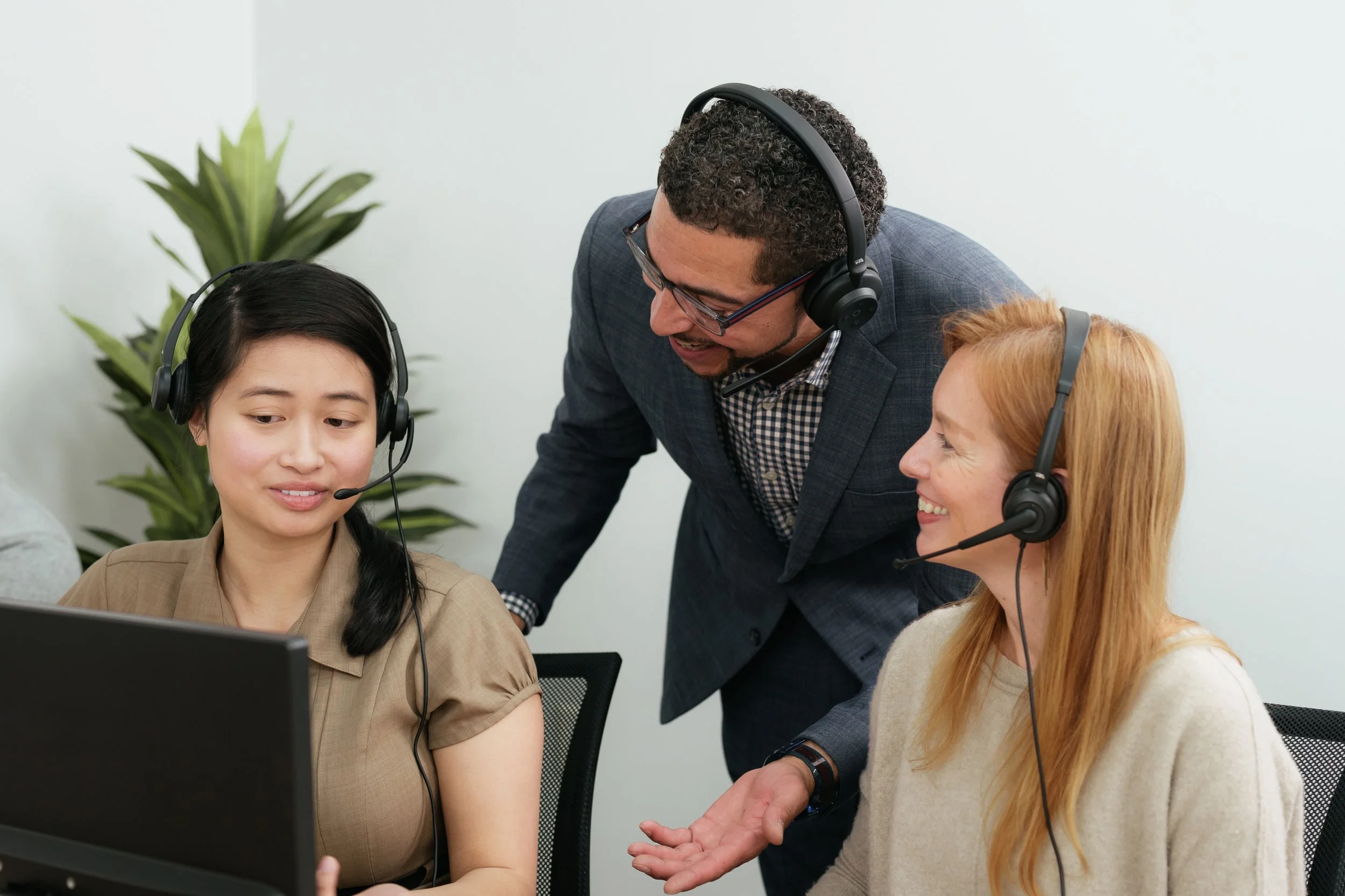 Three call center employees wearing Cyber Acoustics headsets at a shared workstation