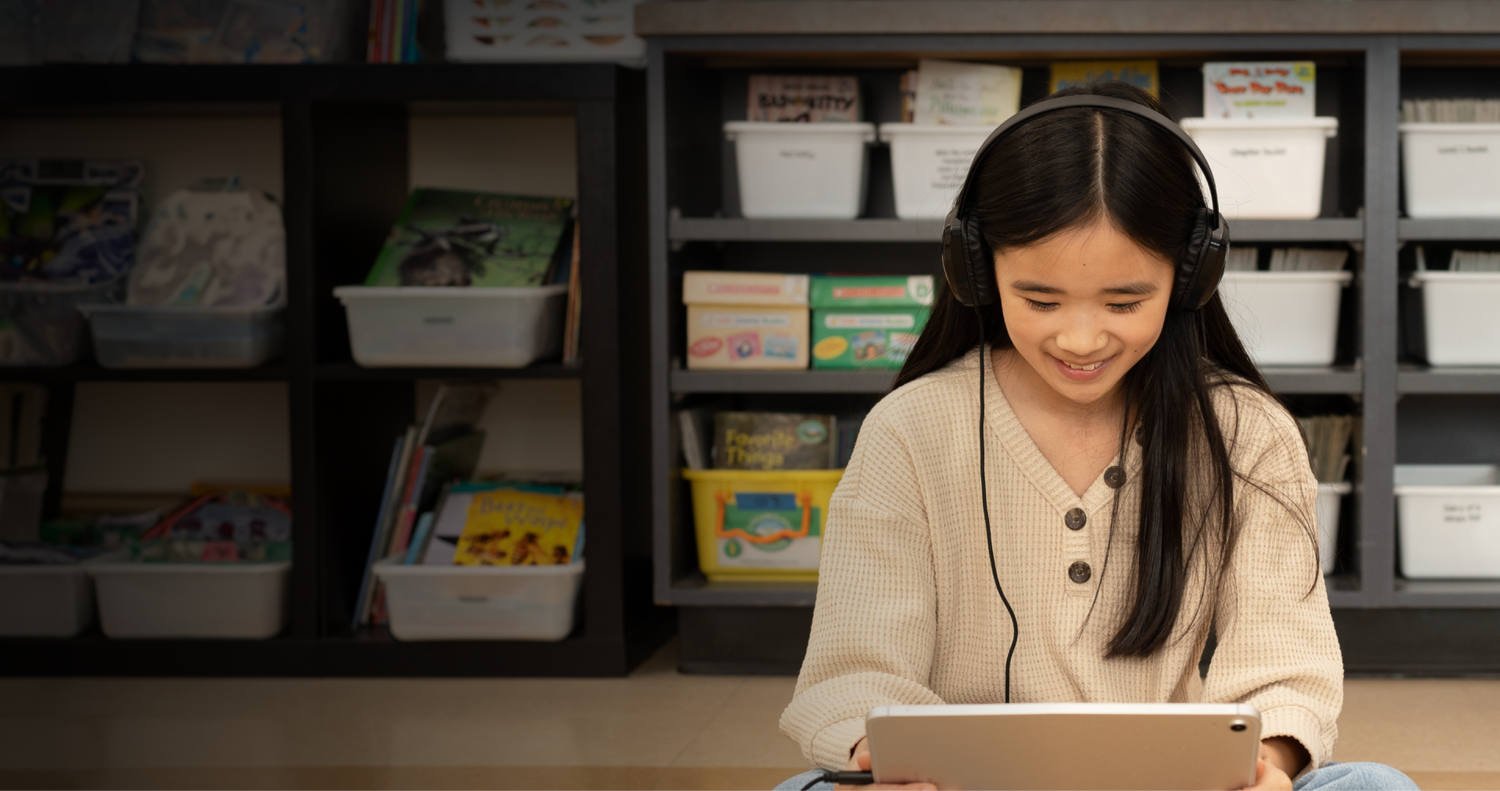 Student wearing headphones smiling while working on a laptop in a classroom