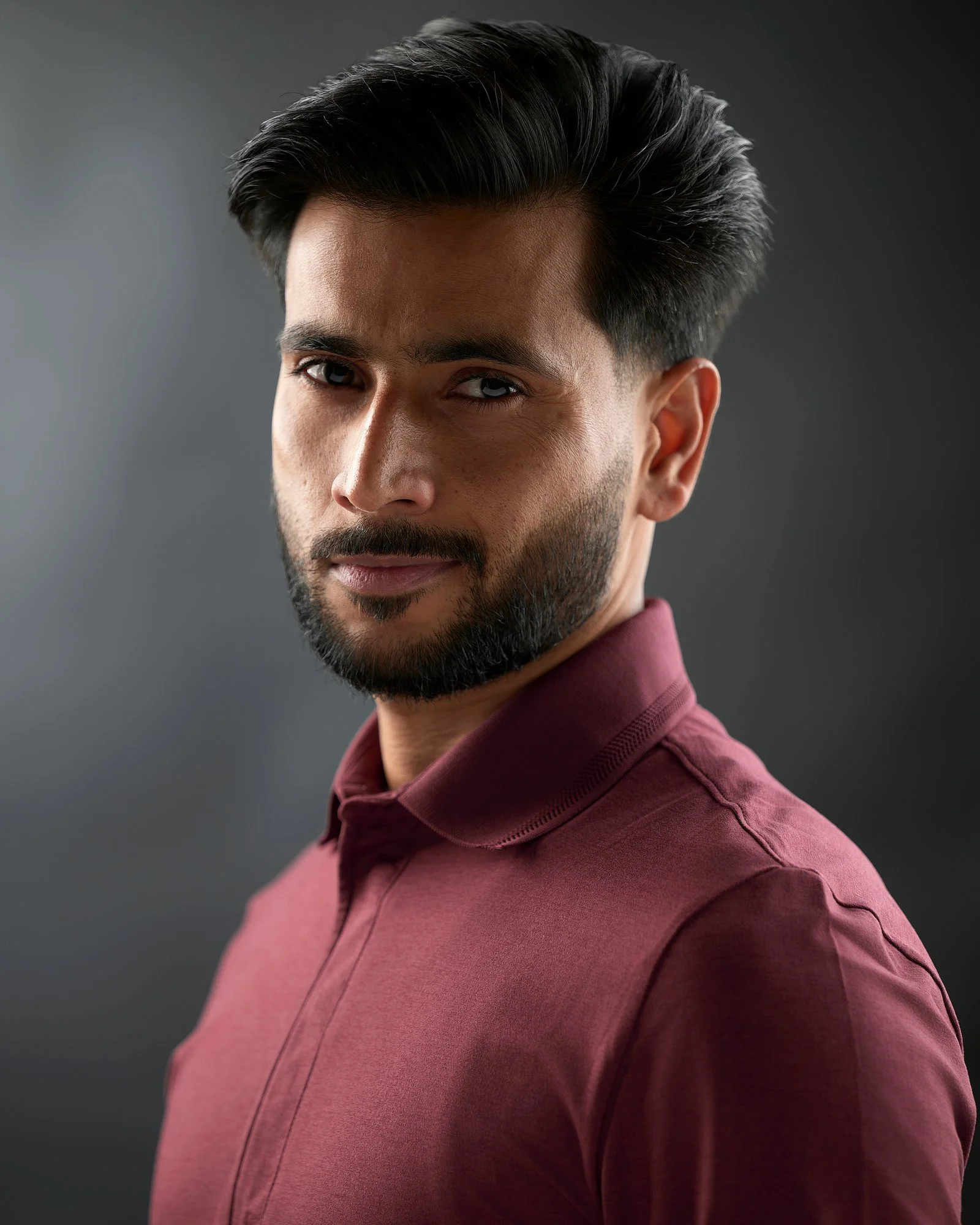 Actor in a burgundy shirt with dramatic side lighting on grey
