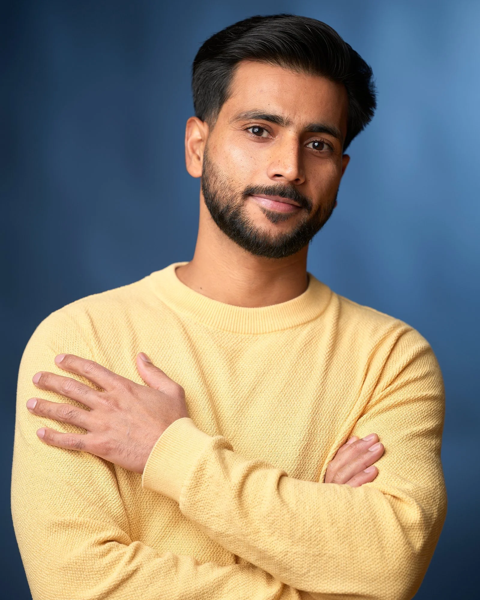 Actor in a yellow sweater with arms crossed on a blue backdrop