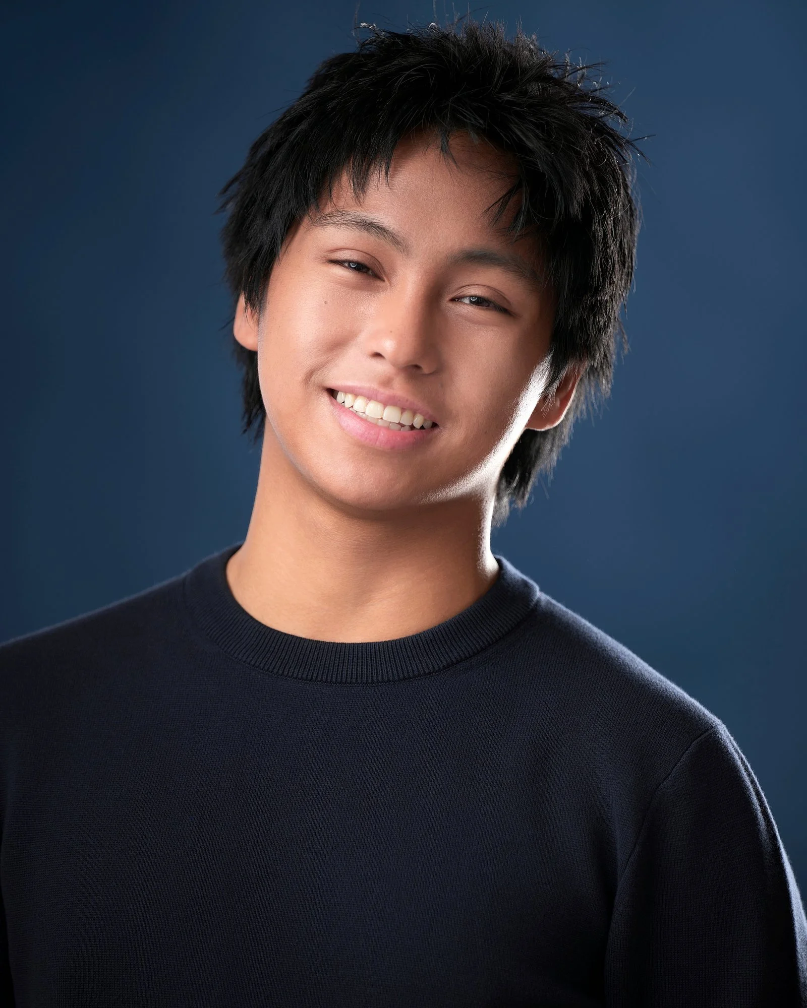 Smiling young actor in a navy sweater on a blue backdrop