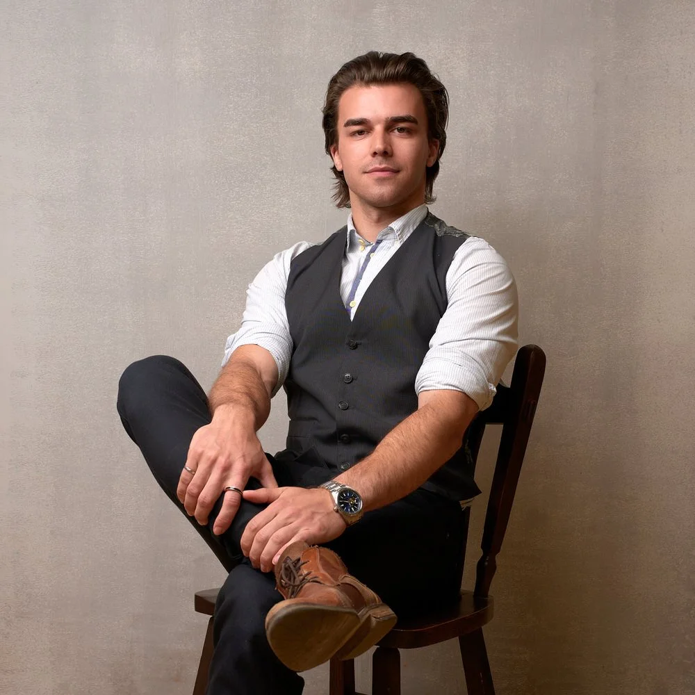 Actor in a waistcoat seated against a warm backdrop
