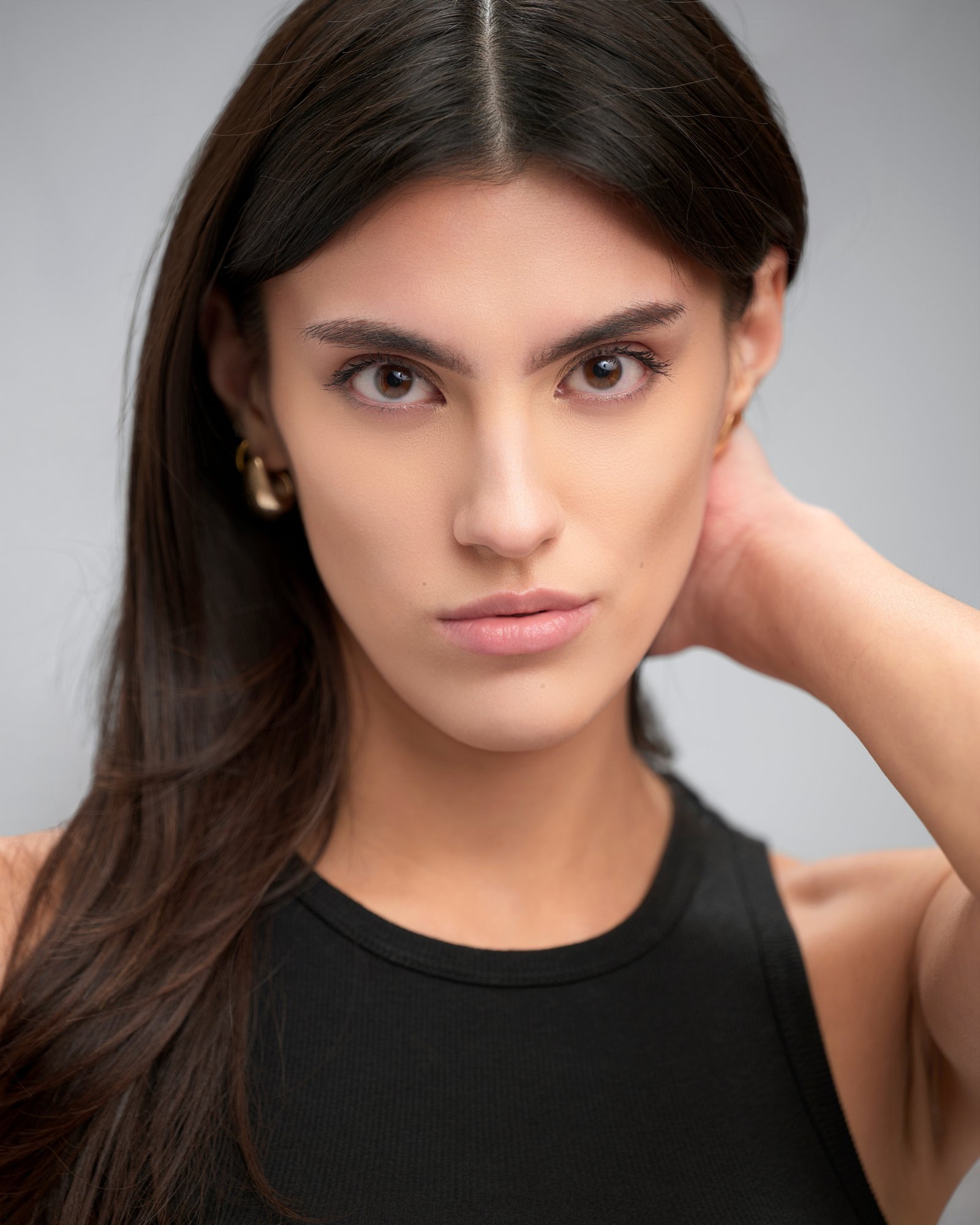 Model headshot in a black tank with a hand behind her neck on light grey