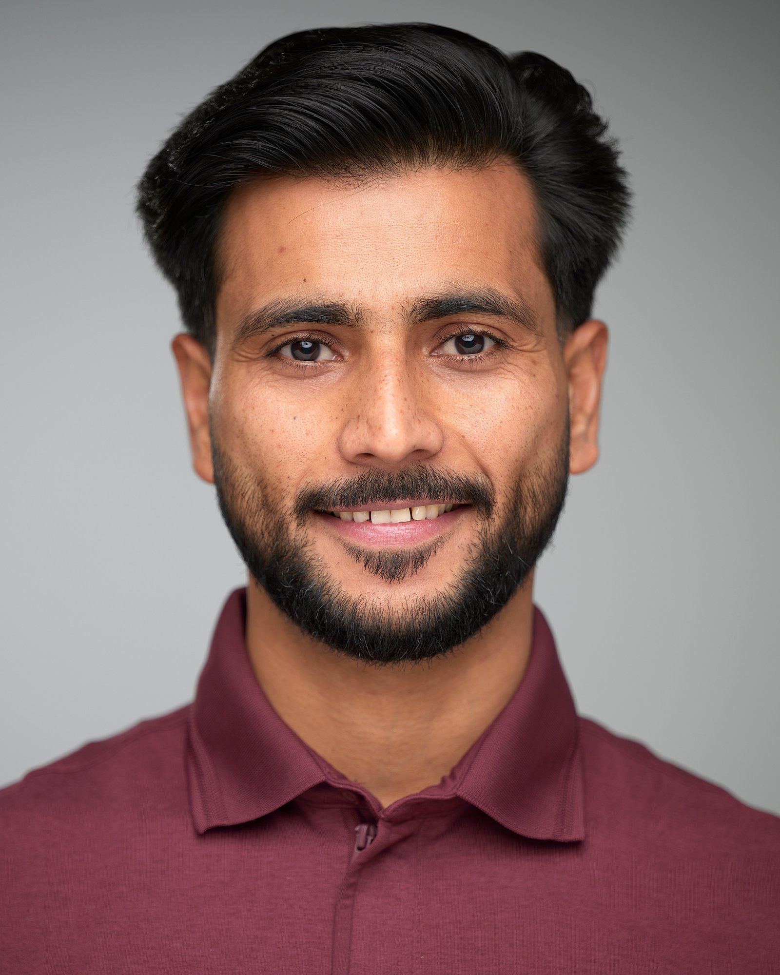 Smiling actor in a burgundy polo on a light grey backdrop