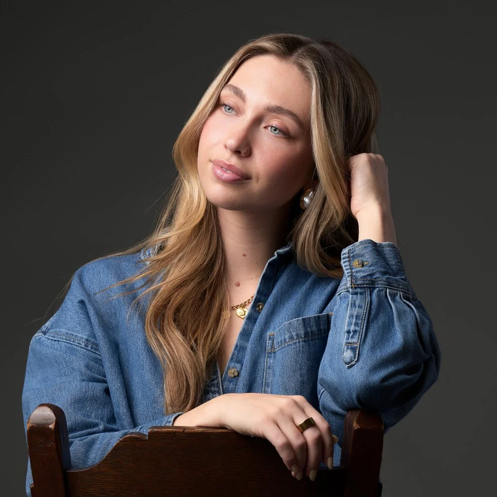 Actor in a denim shirt seated against a dark backdrop