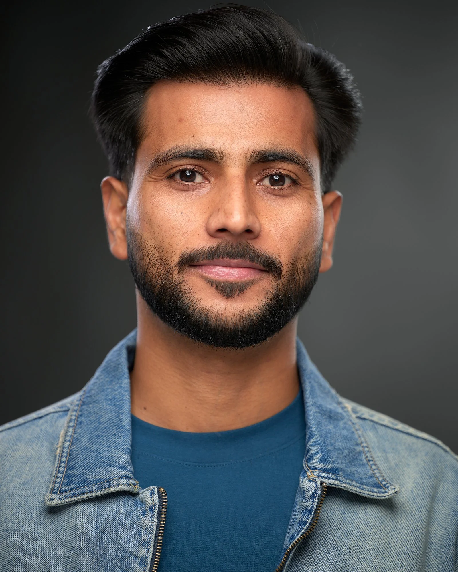 Actor in a denim jacket and blue tee, close-up on a dark grey backdrop