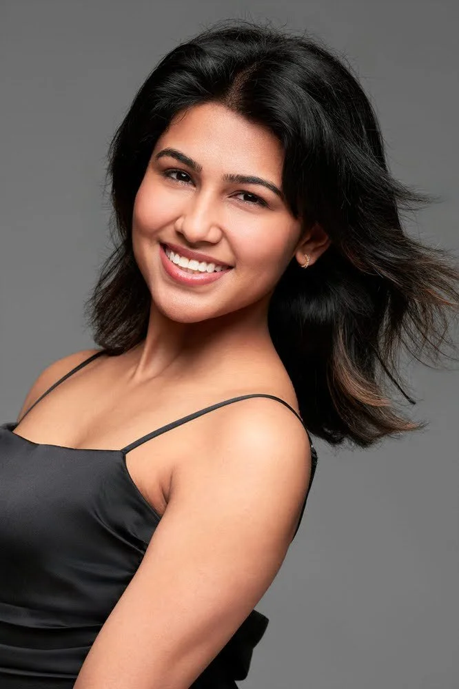 Smiling model headshot in a black strap top on grey