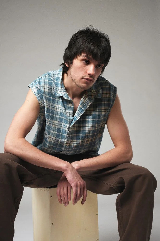 Male model in a plaid shirt seated against grey