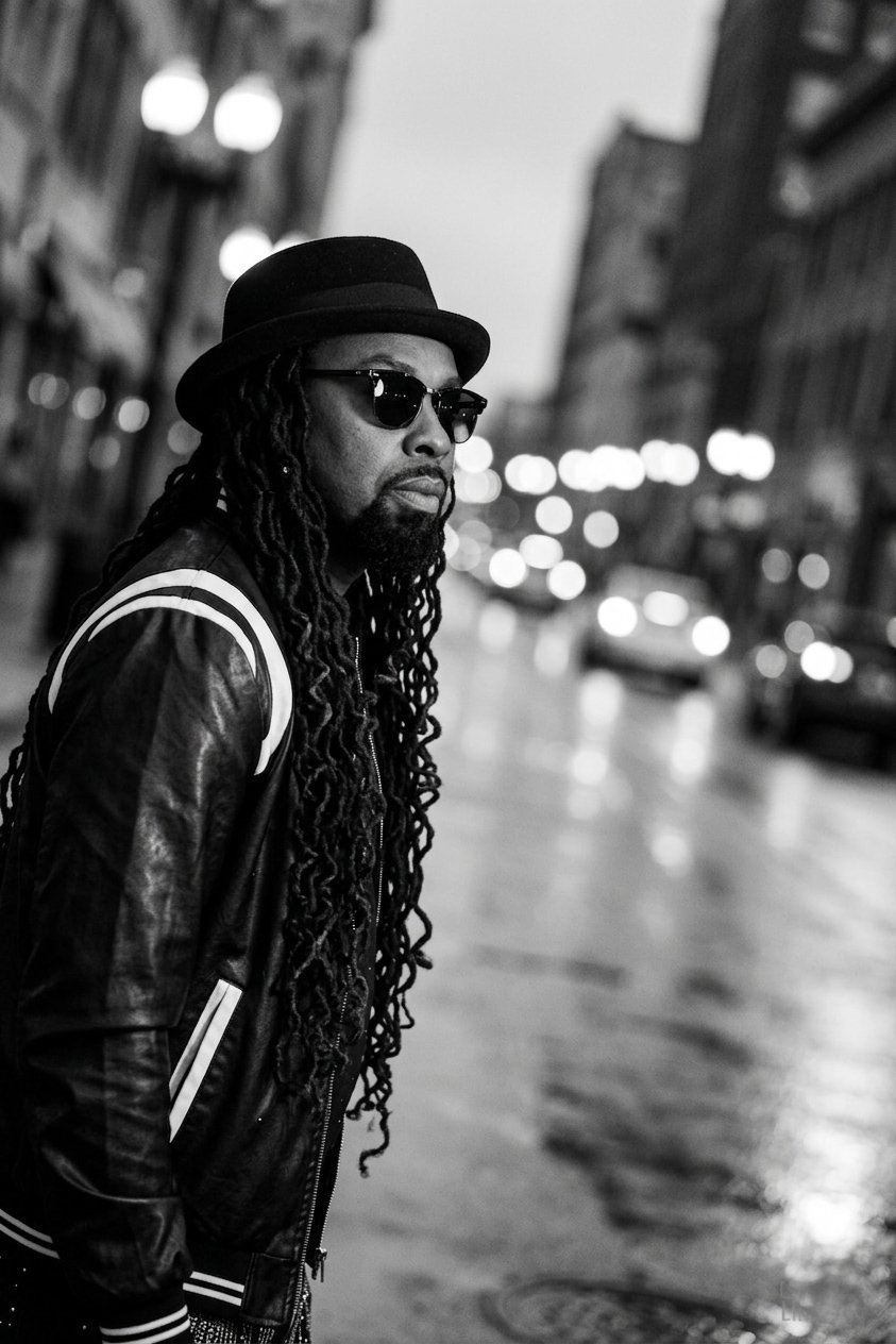 Brayo in a hat and shades on a city street