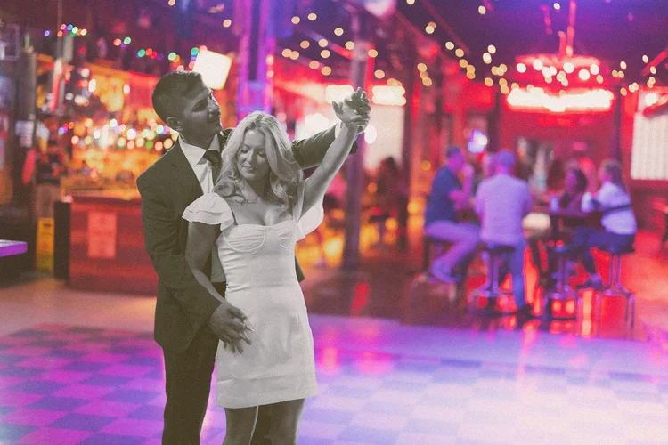 A black and white portrait of a couple mid twirl on a checkerboard dance floor under neon at the Hoxton Chicago, by Jeremy Glickstein