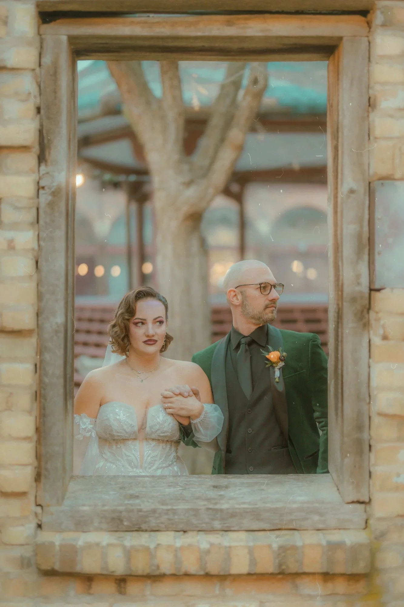 Wes Anderson style wedding photo with couple framed by rustic brick window creating symmetrical composition