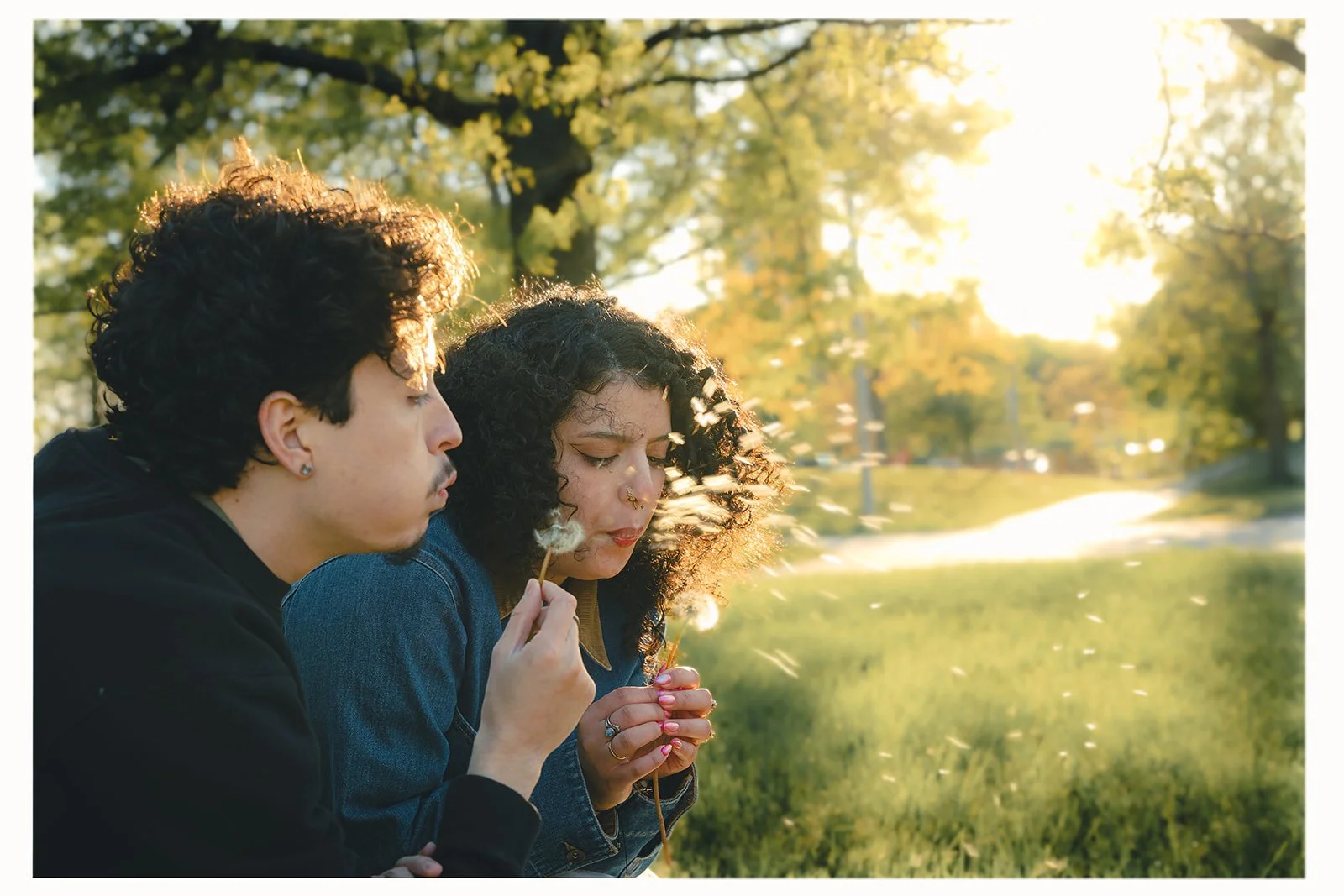 Miguel and Ally blowing dandelion seed heads together at golden hour, cinematic and playful