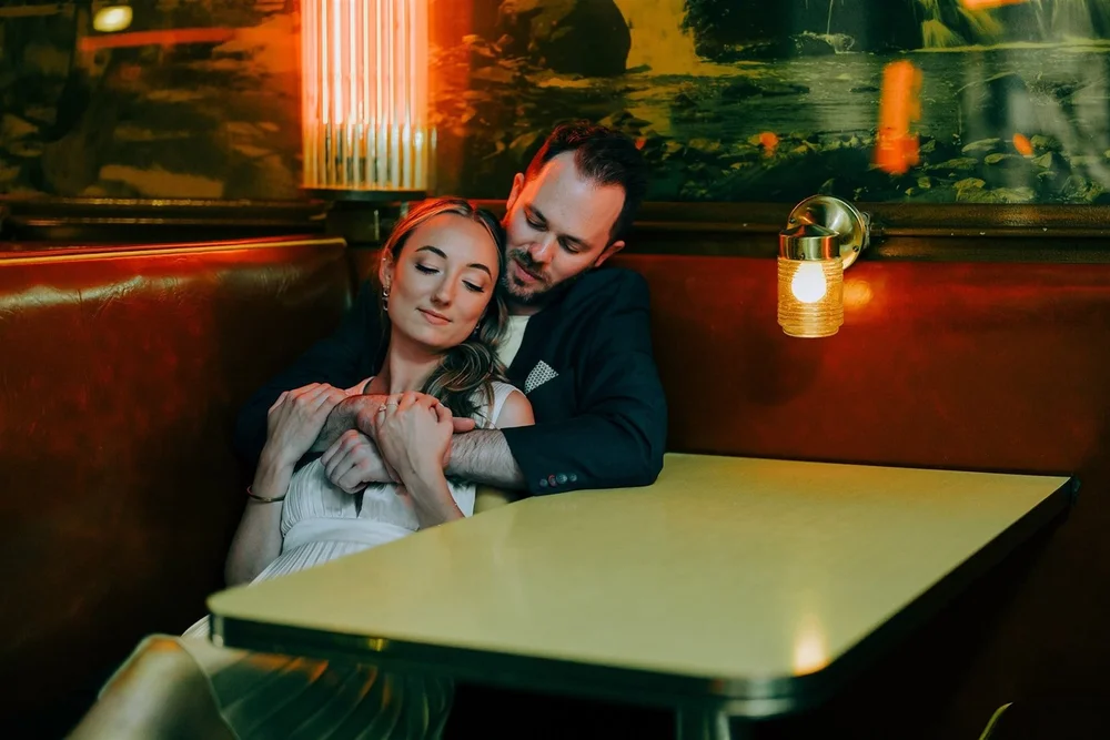 A couple settled into a dim vintage diner booth, a cinematic portrait by Jeremy Glickstein, Chicago proposal and wedding photographer