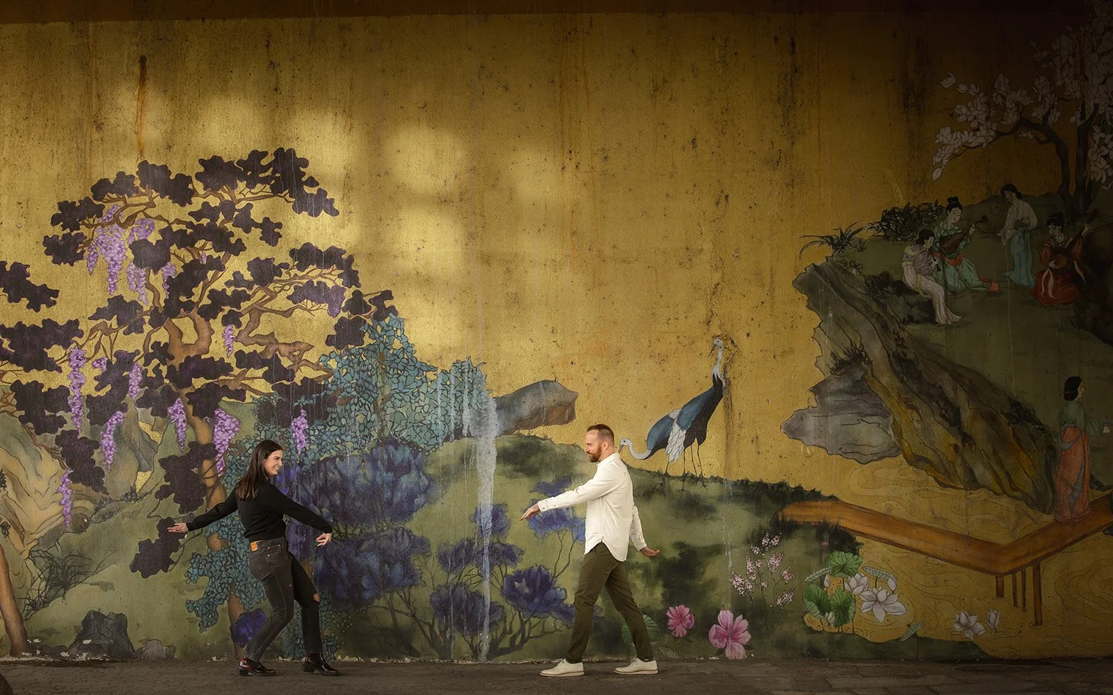 Fun Chicago engagement photos showing playful couple reaching for each other in front of colorful Chinatown mural