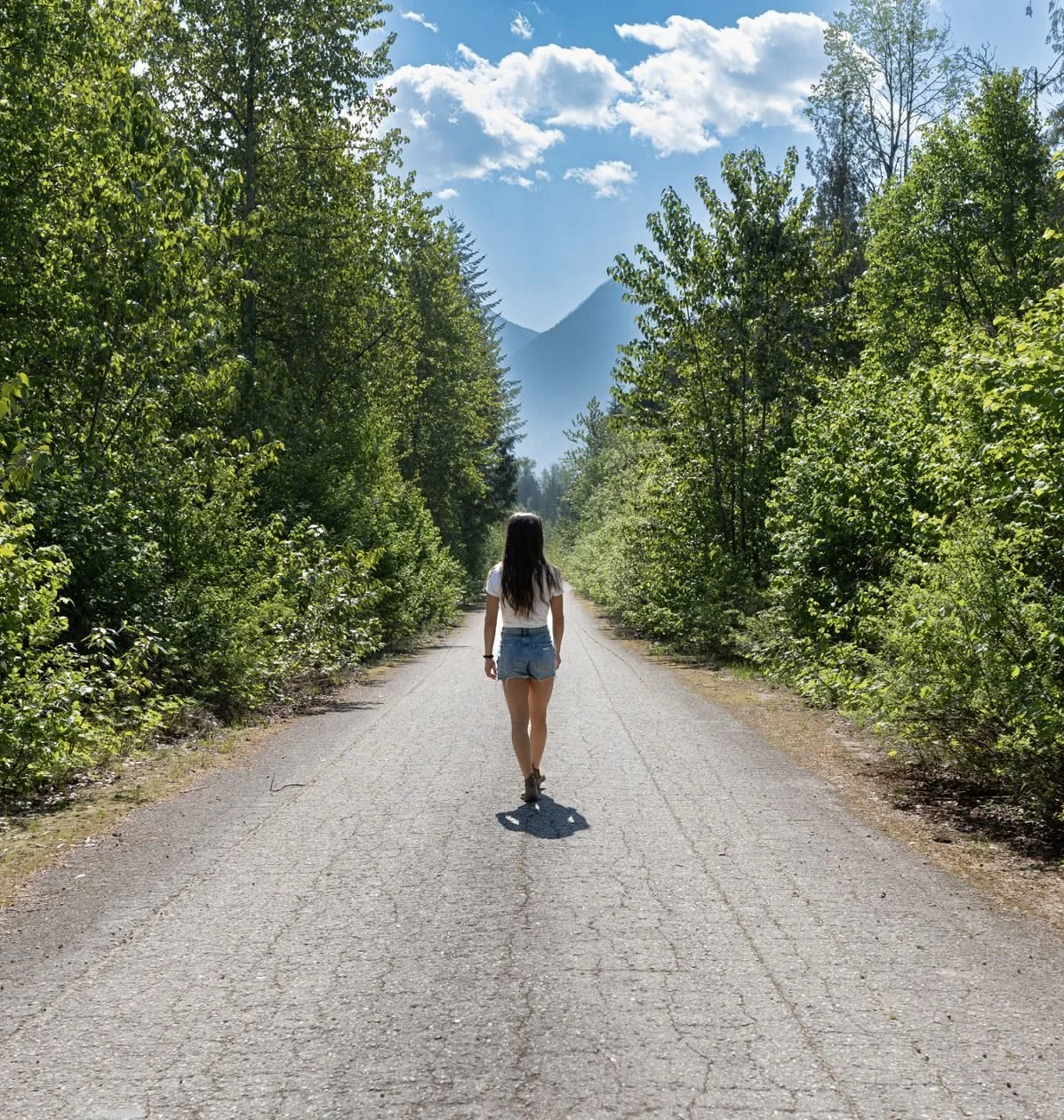 A guest walking down the cracked, tree-lined pavement of the original Trans-Canada Highway at the back of Crazy Creek, mountains ahead