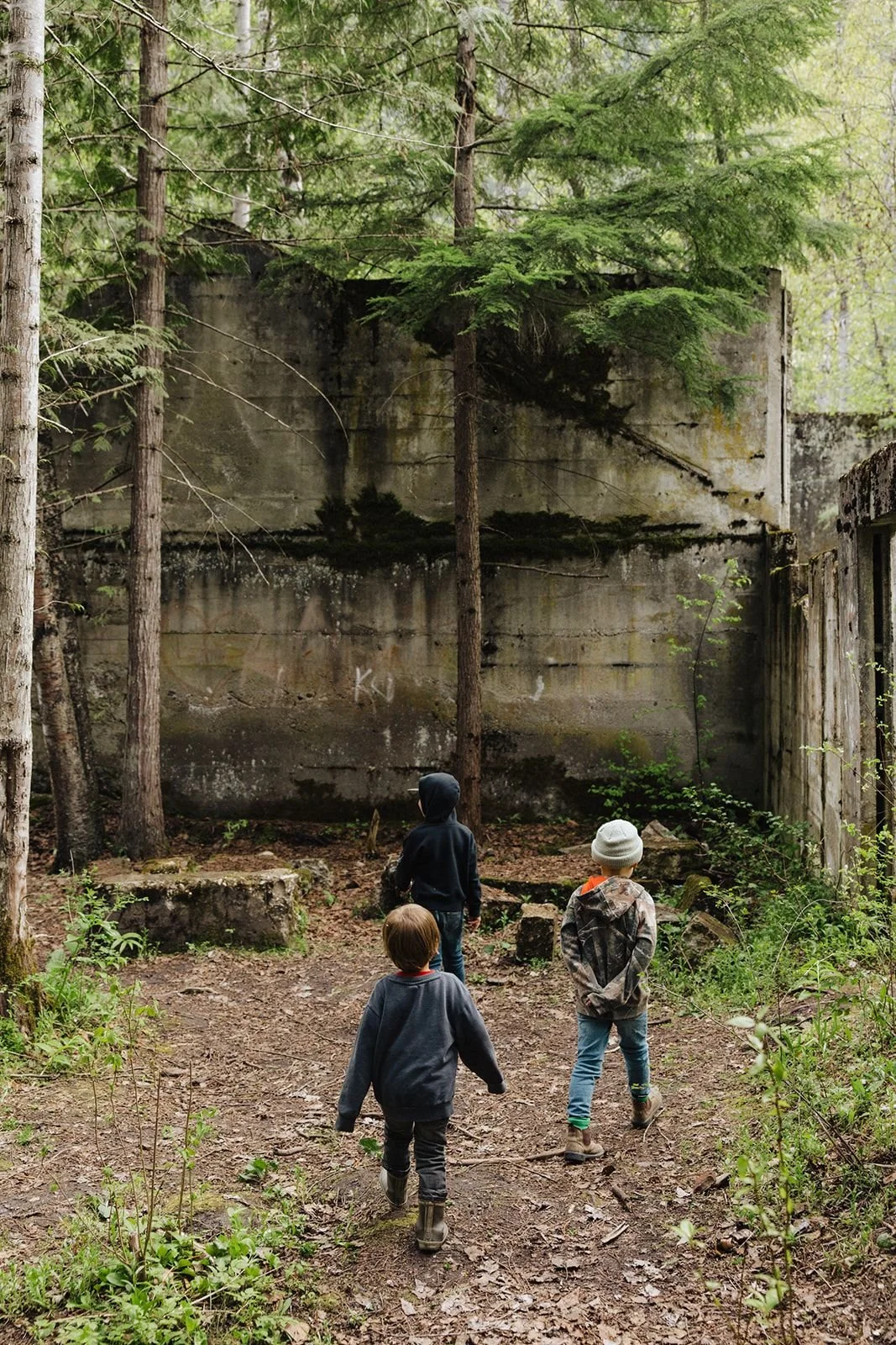 Two young kids walking through the forest toward the moss-covered concrete ruins of the old Taft sawmill