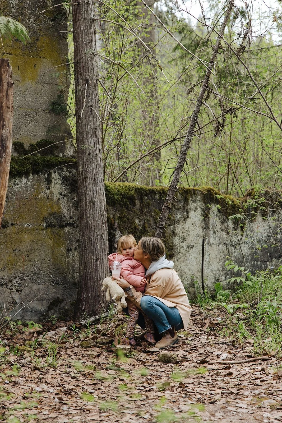 A mother hugging her toddler beside a moss-covered concrete wall of the Taft ruins in the forest