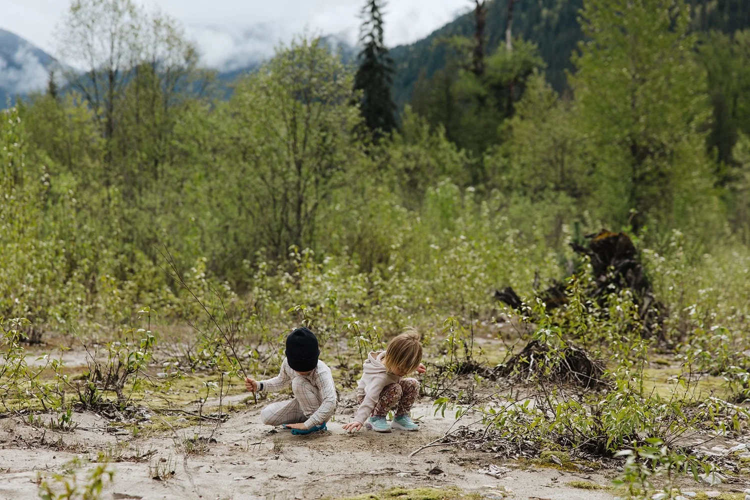 Two toddlers playing in the sand on the Eagle River flats at Crazy Creek, mountains and cloud behind