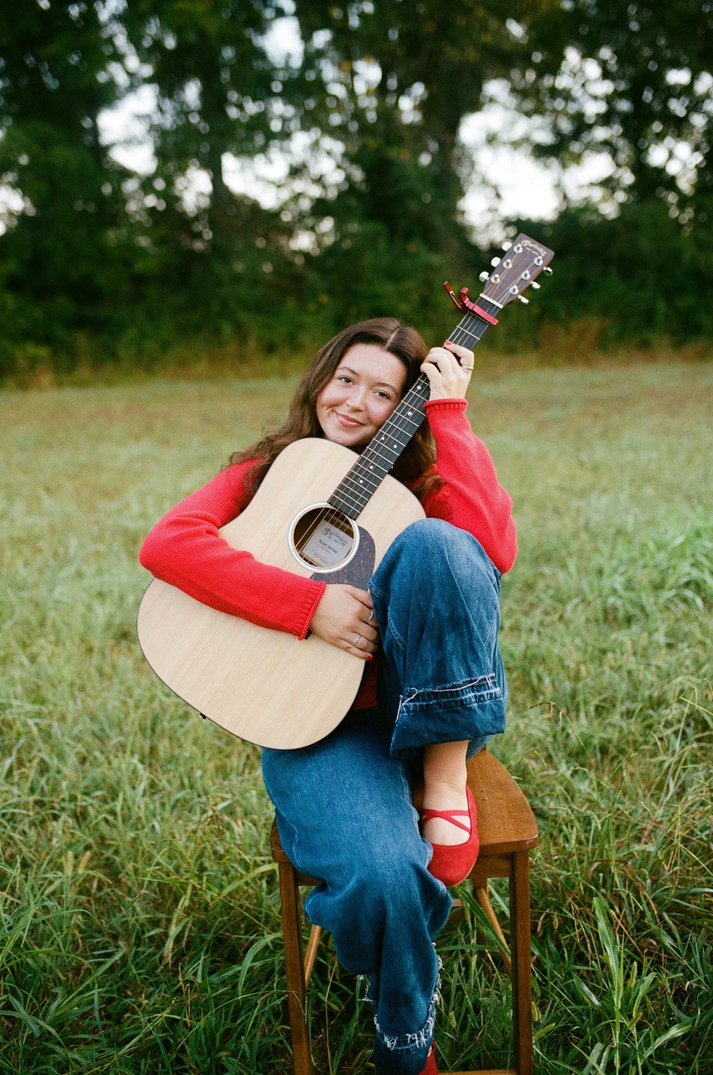 press photo: Katie seated on a stool with her guitar