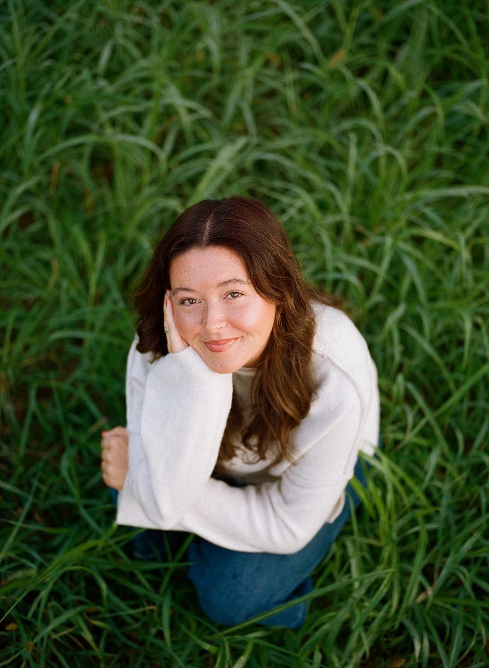 press photo: Katie smiling up at the camera in tall grass