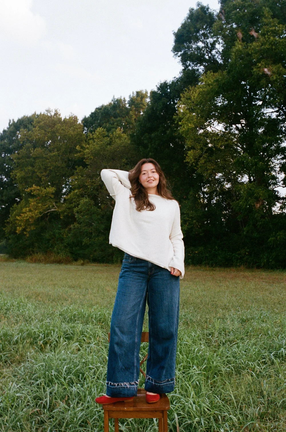 katie flemming in a cream sweater standing on a chair in a field