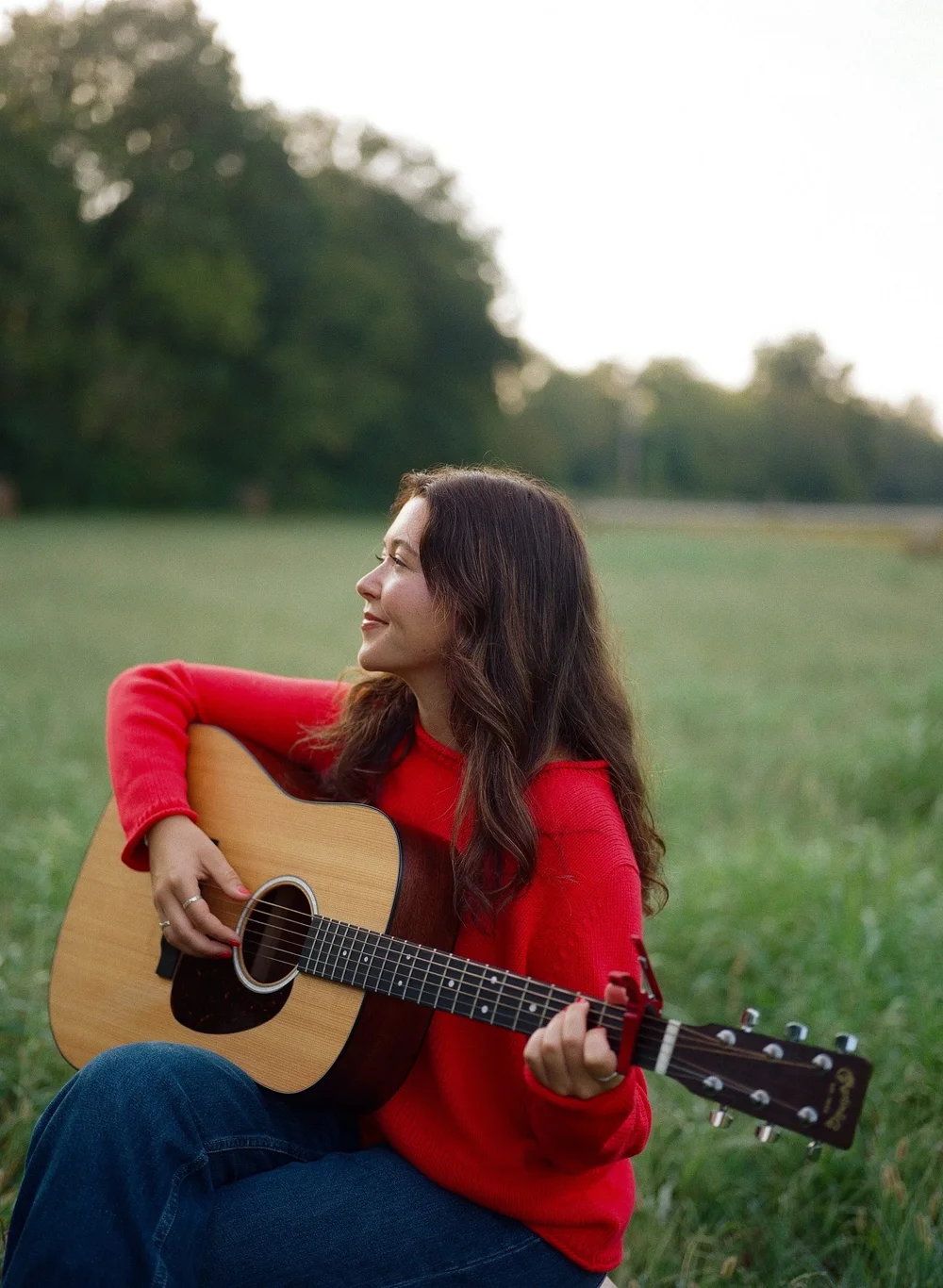 katie flemming smiling with her acoustic guitar in a field