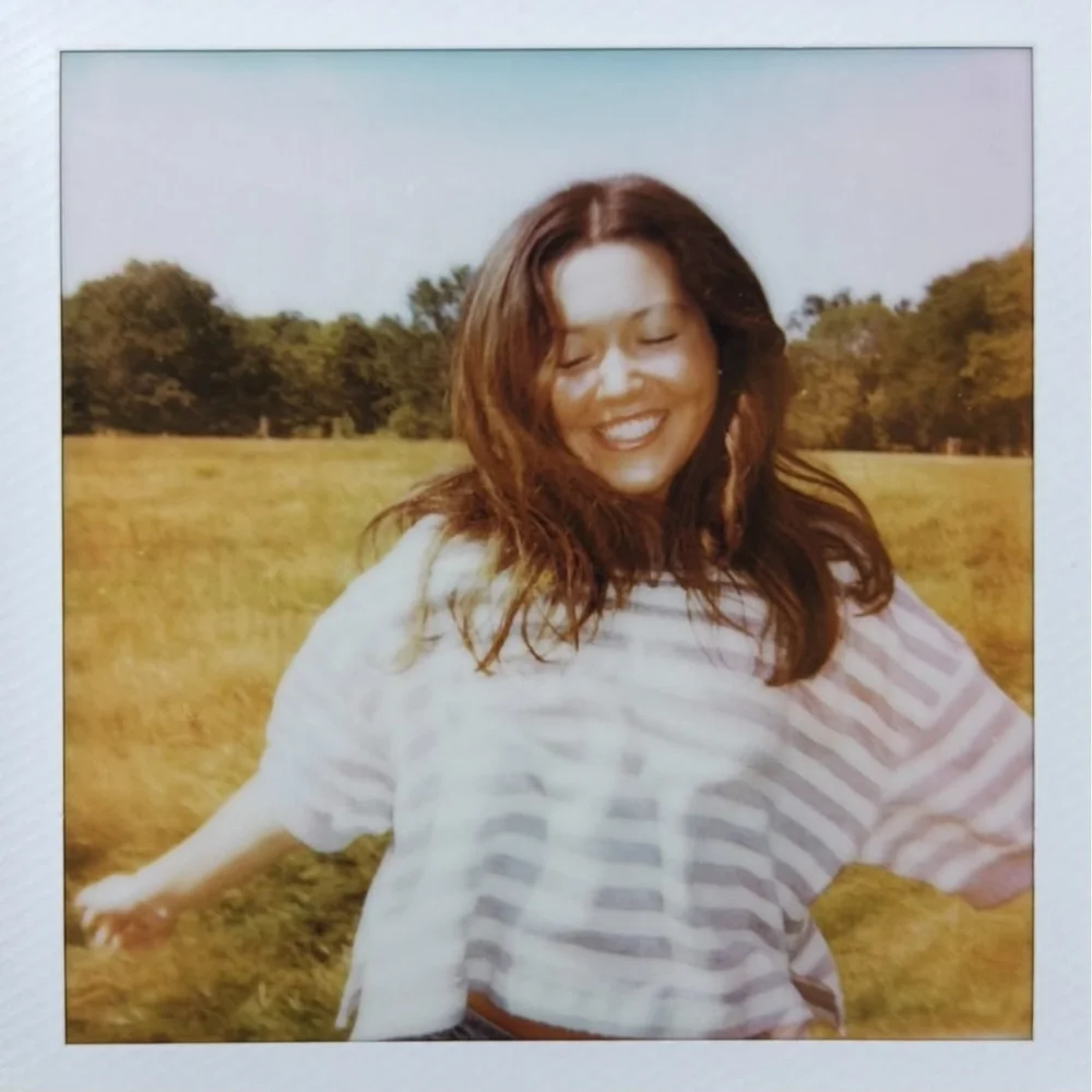 a polaroid of katie laughing in a field