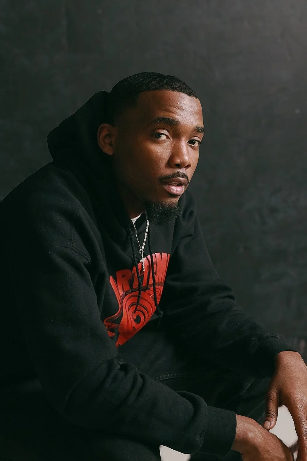 Seated portrait in a dark hoodie