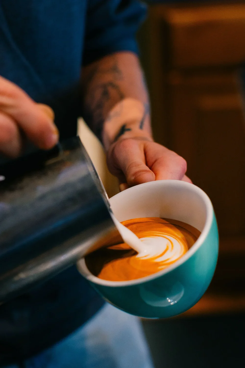 A barista pouring latte art into a teal cup at Turnstile Coffee