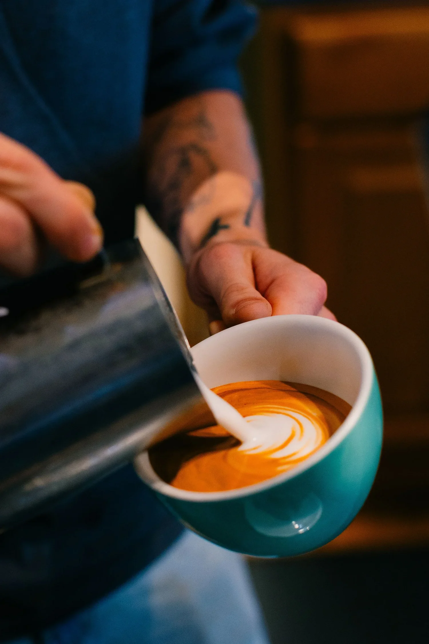 A barista pouring latte art into a teal cup at Turnstile Coffee