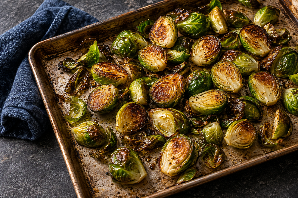 Halved roasted Brussels sprouts with browned faces on a metal tray beside a blue towel