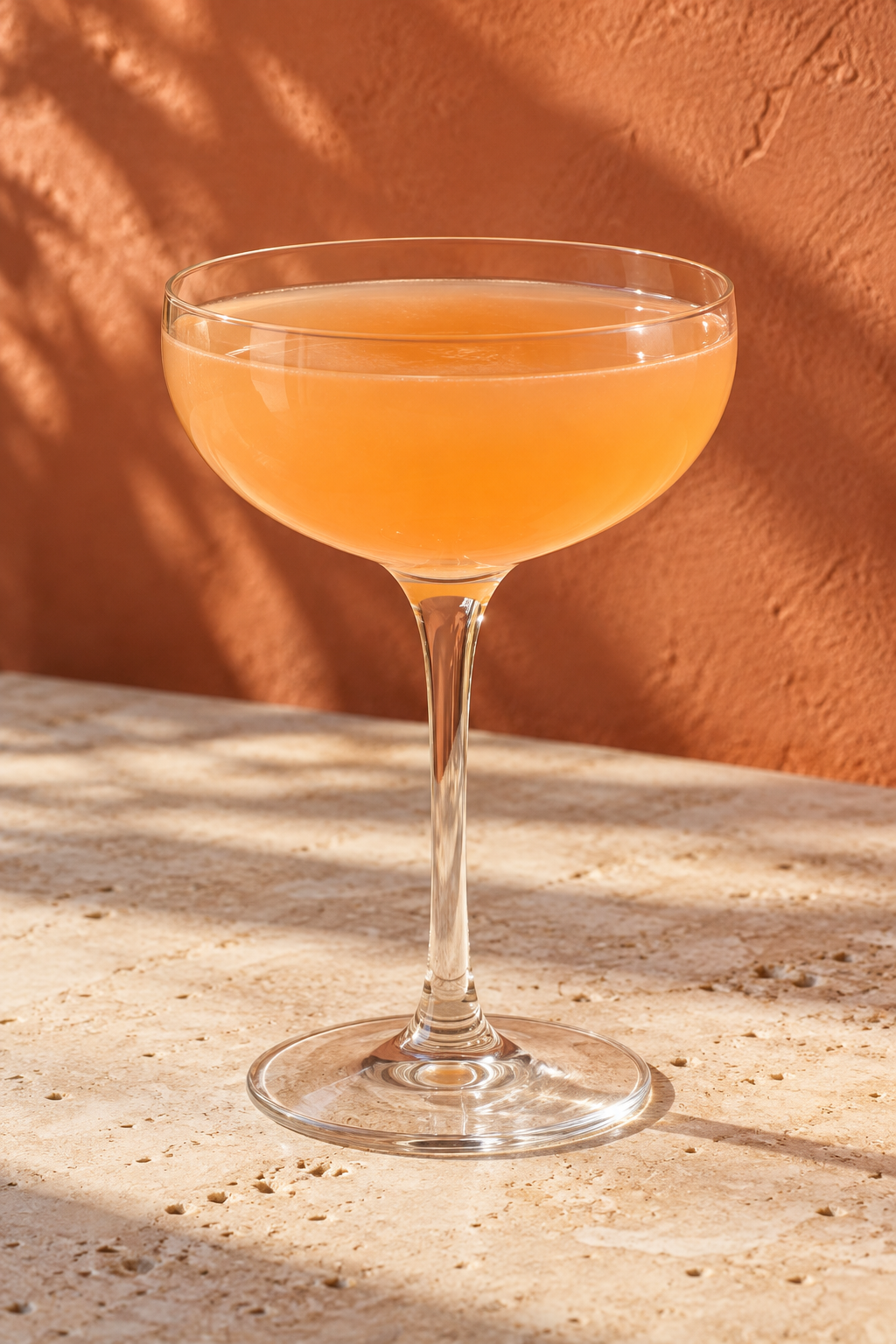 Peach-orange Naked and Famous cocktail without garnish in a coupe on pale travertine