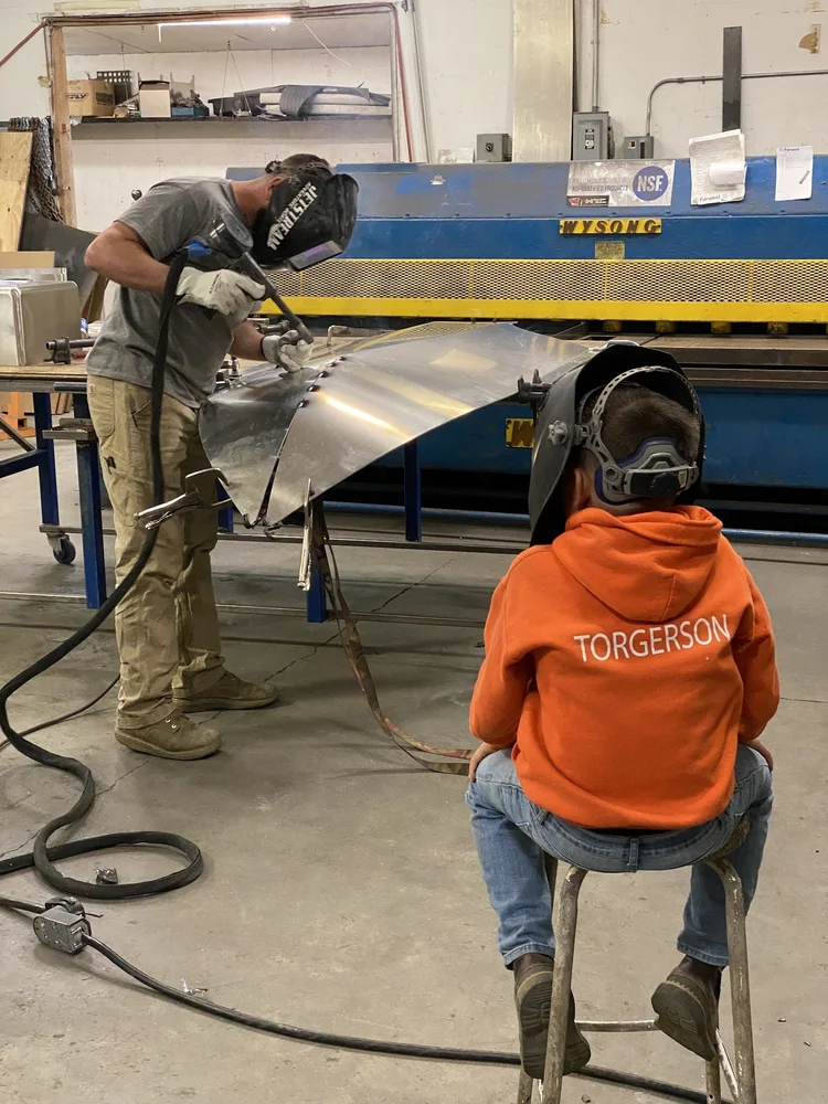 Builder welding an aluminum hull supported on a workshop bench