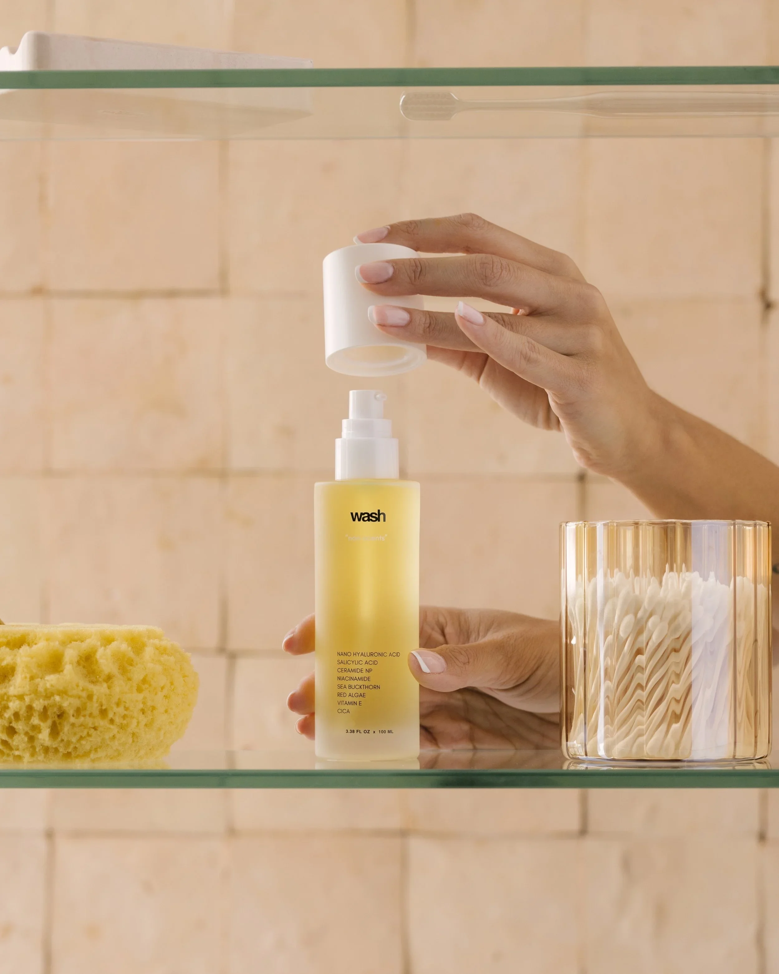 Pluxos Wash facial cleanser on glass bathroom shelf with sponge and cotton swabs, product photography by Matt Francisco Los Angeles