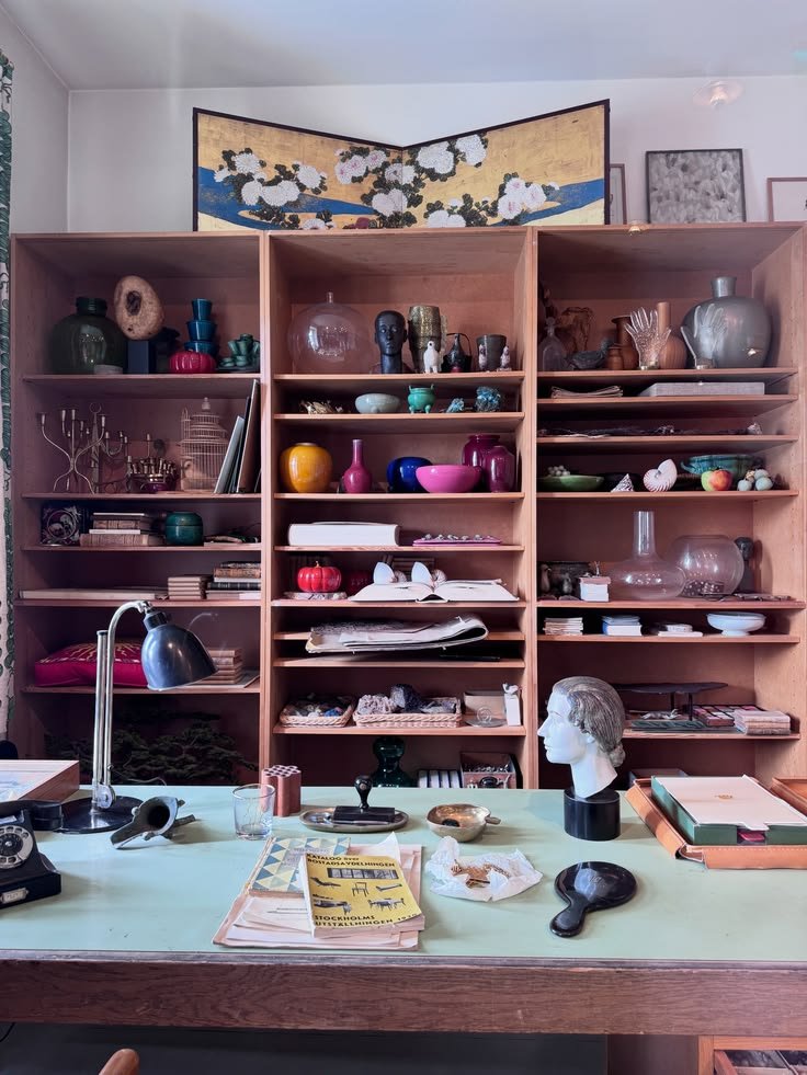 Desk with a pale blue chair and tall wooden shelves holding books, ceramics, and small objects at Svenskt Tenn.