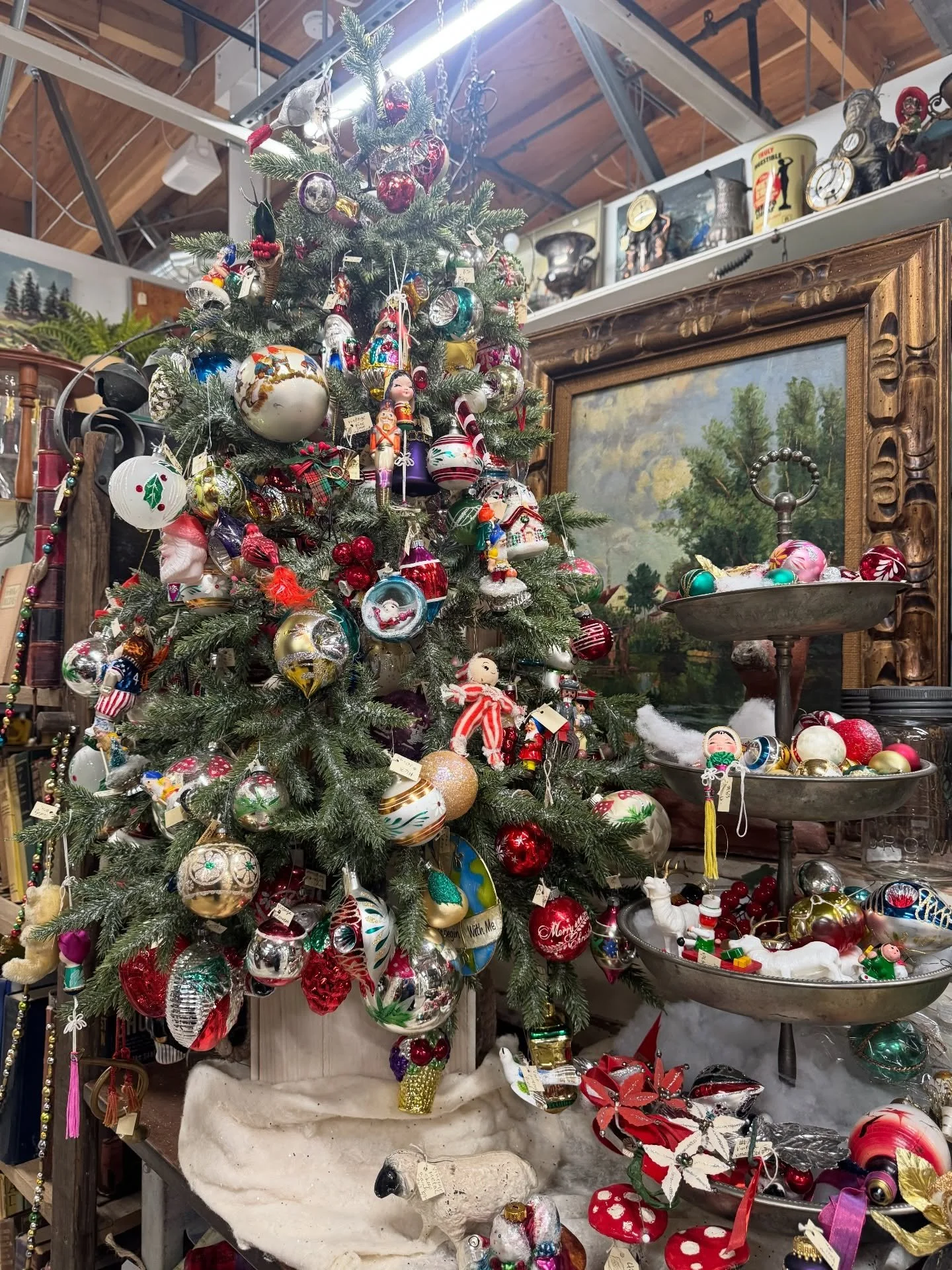 Decorated Christmas tree surrounded by vintage objects in a shop.