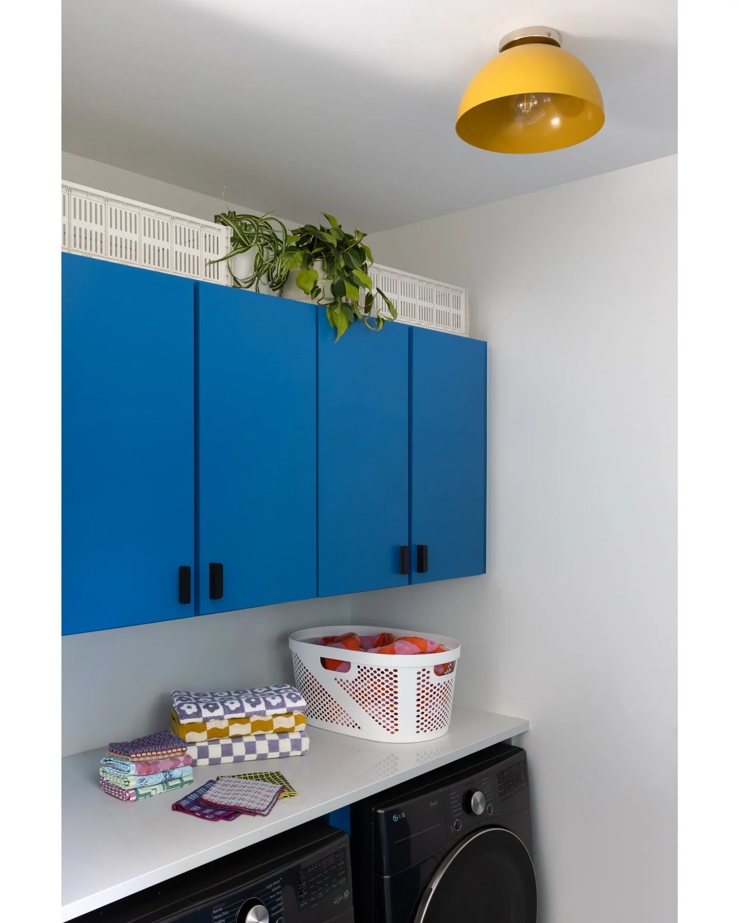 Mudroom with cobalt wall cabinets, a white counter, plants, and a yellow pendant light.