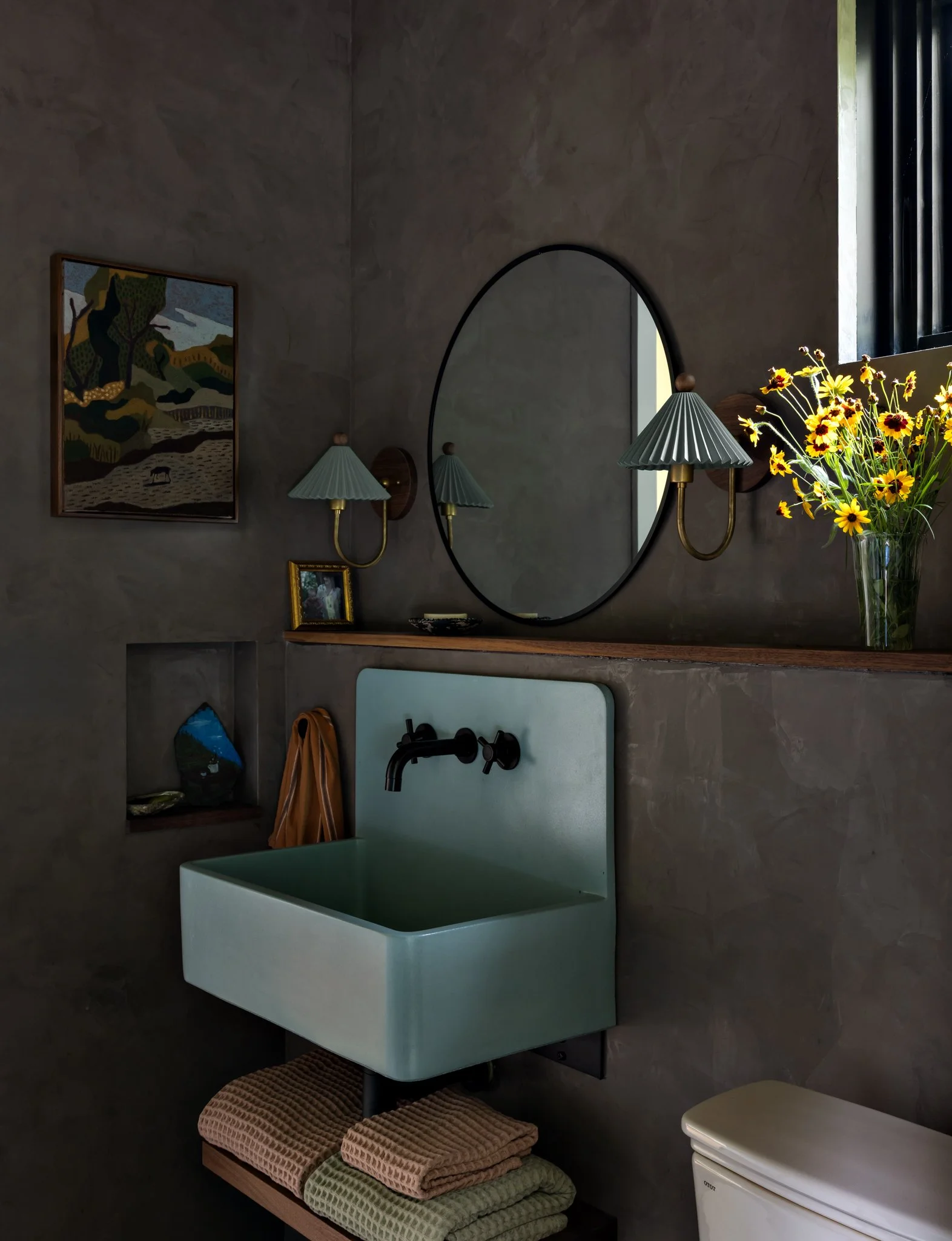 Guest-house bathroom with a pale green wall-mounted sink, dark wall faucet, oval mirror, textured walls, and pleated sconces.