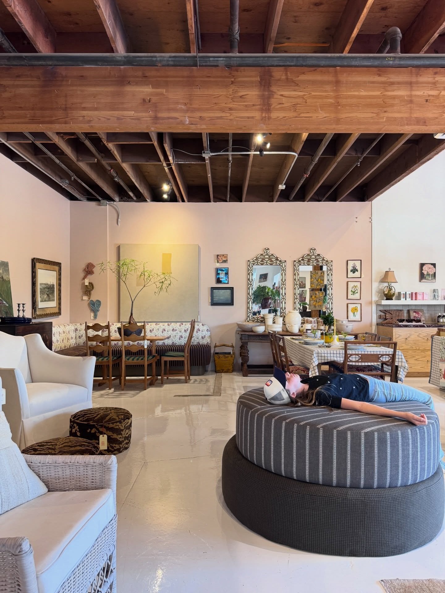 Vintage showroom with exposed timber ceiling, upholstered seating, wood furniture, and framed art.