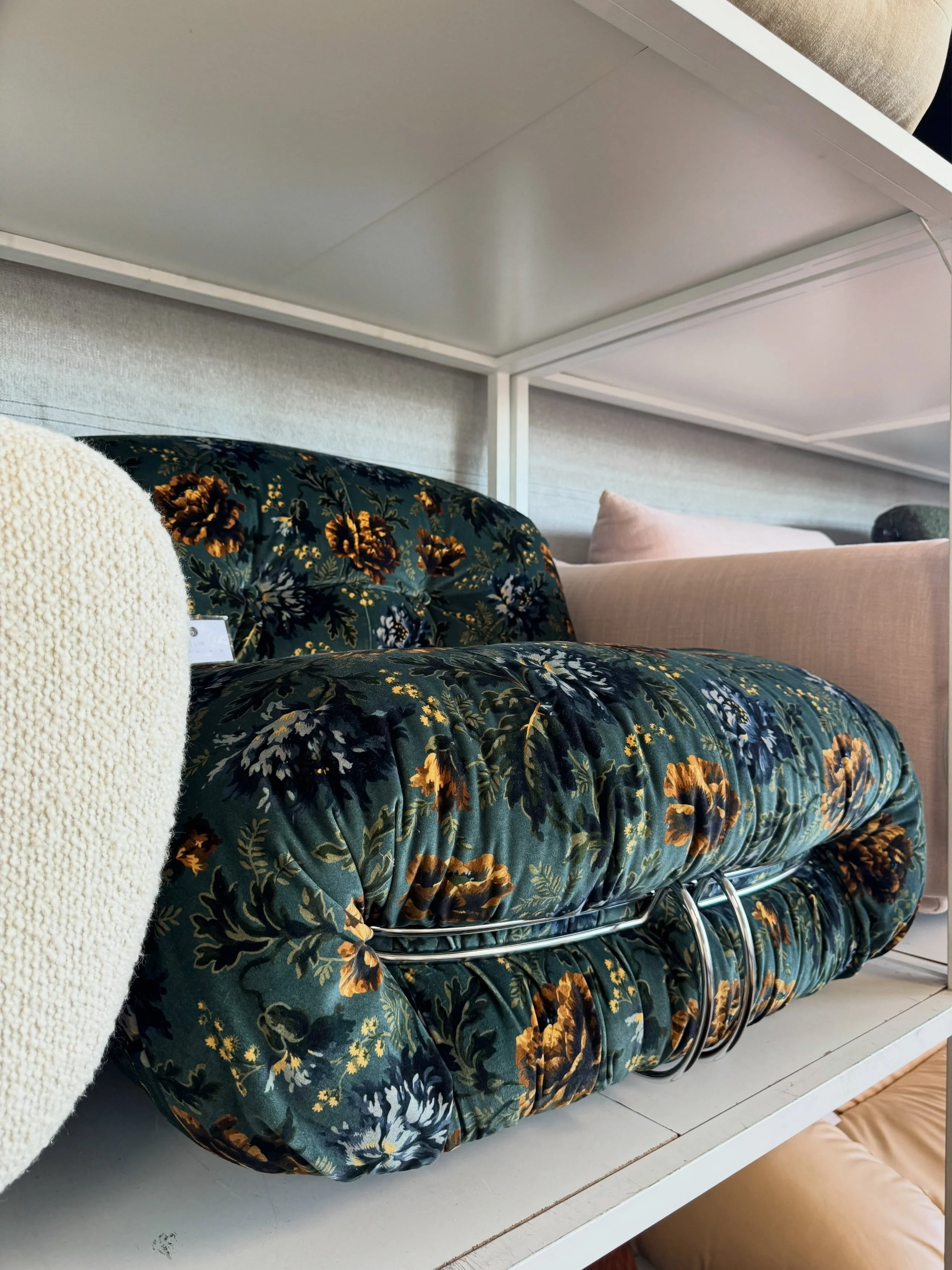 Sofa upholstered in a dark botanical fabric, displayed beside pale upholstered seating.