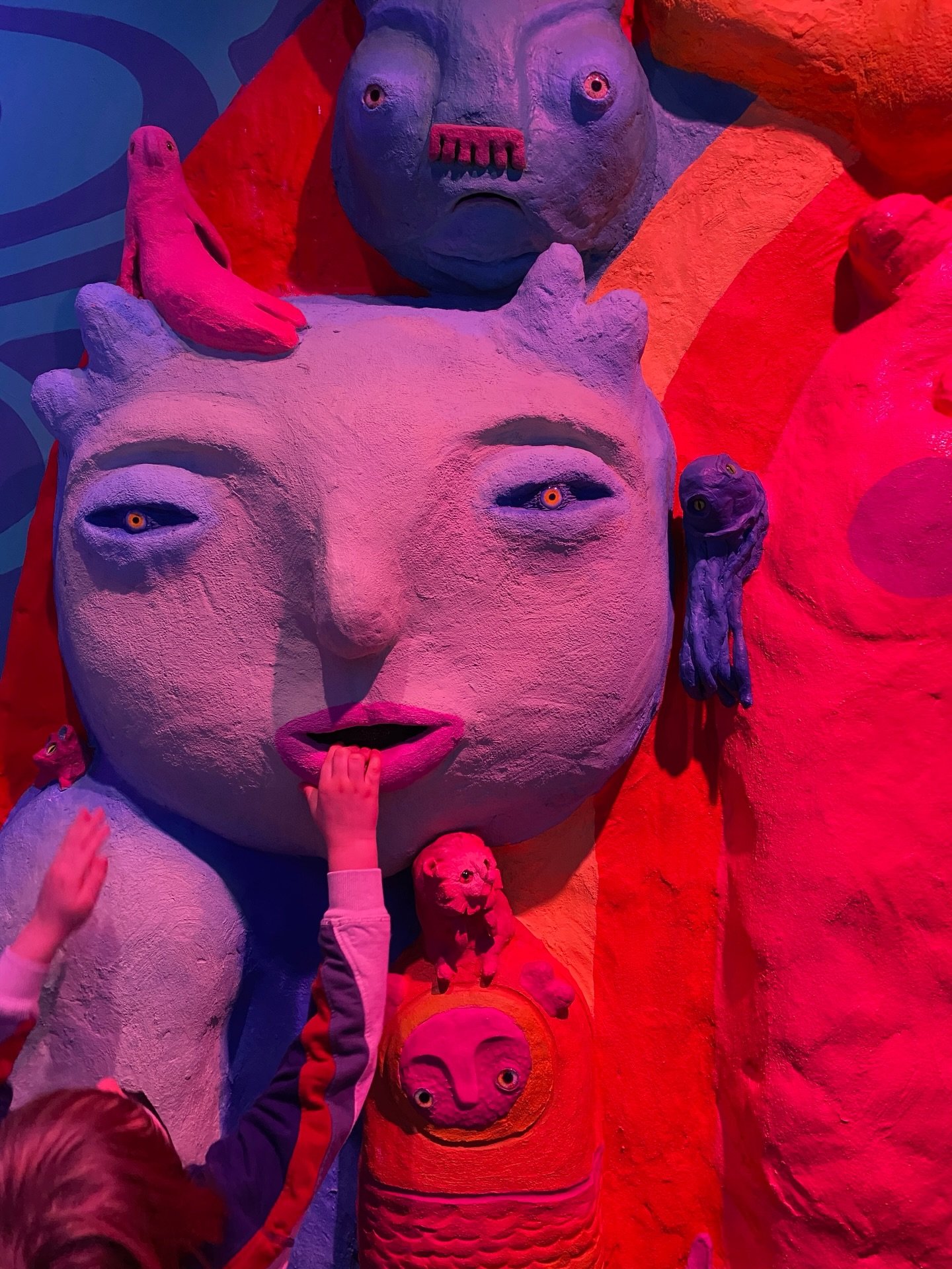 Sculptural faces and figures illuminated in pink, red, and purple at Meow Wolf Convergence Station.