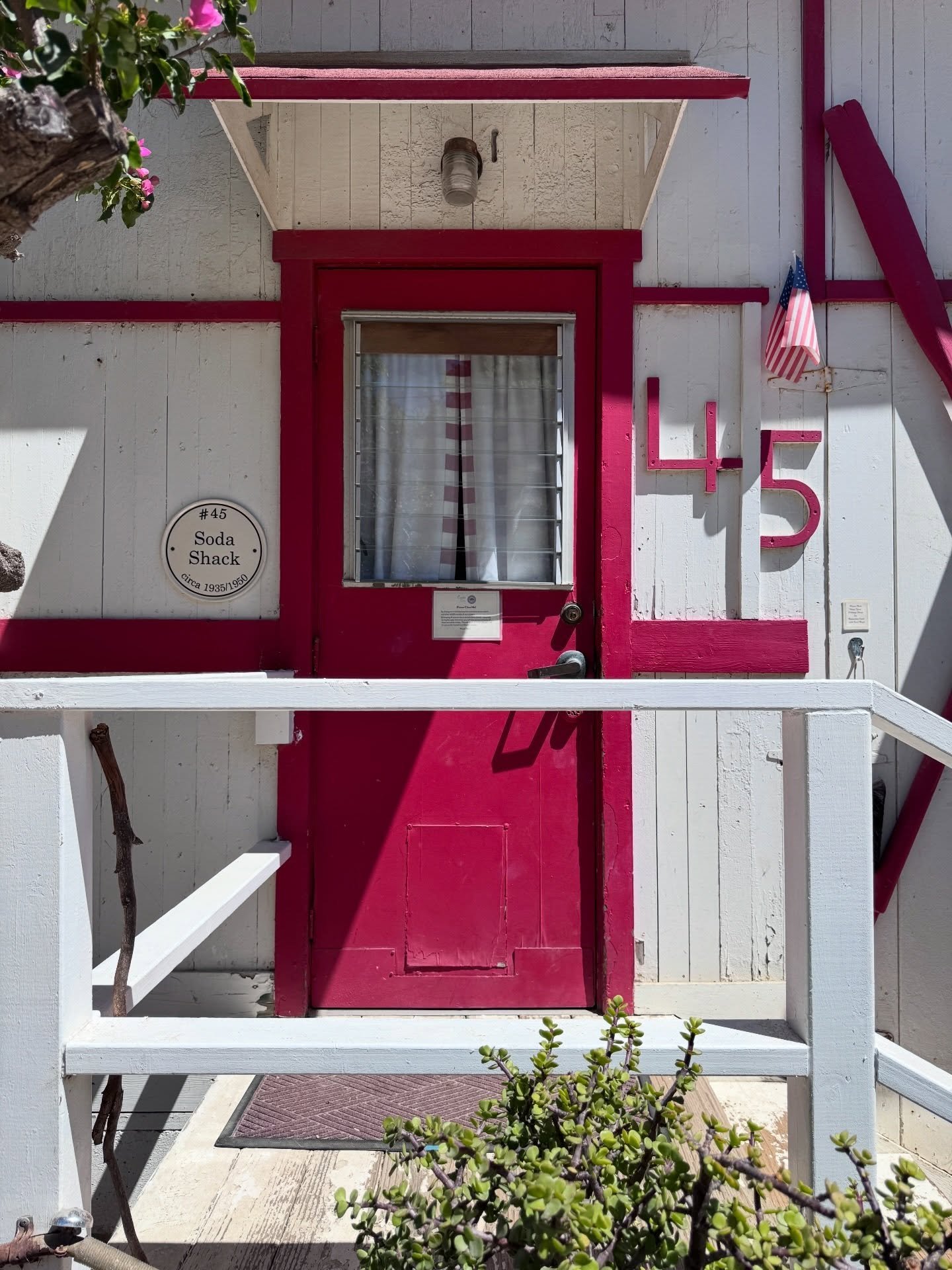 Coastal cottage porch with a red screen door, white timber details, and a garden gate.