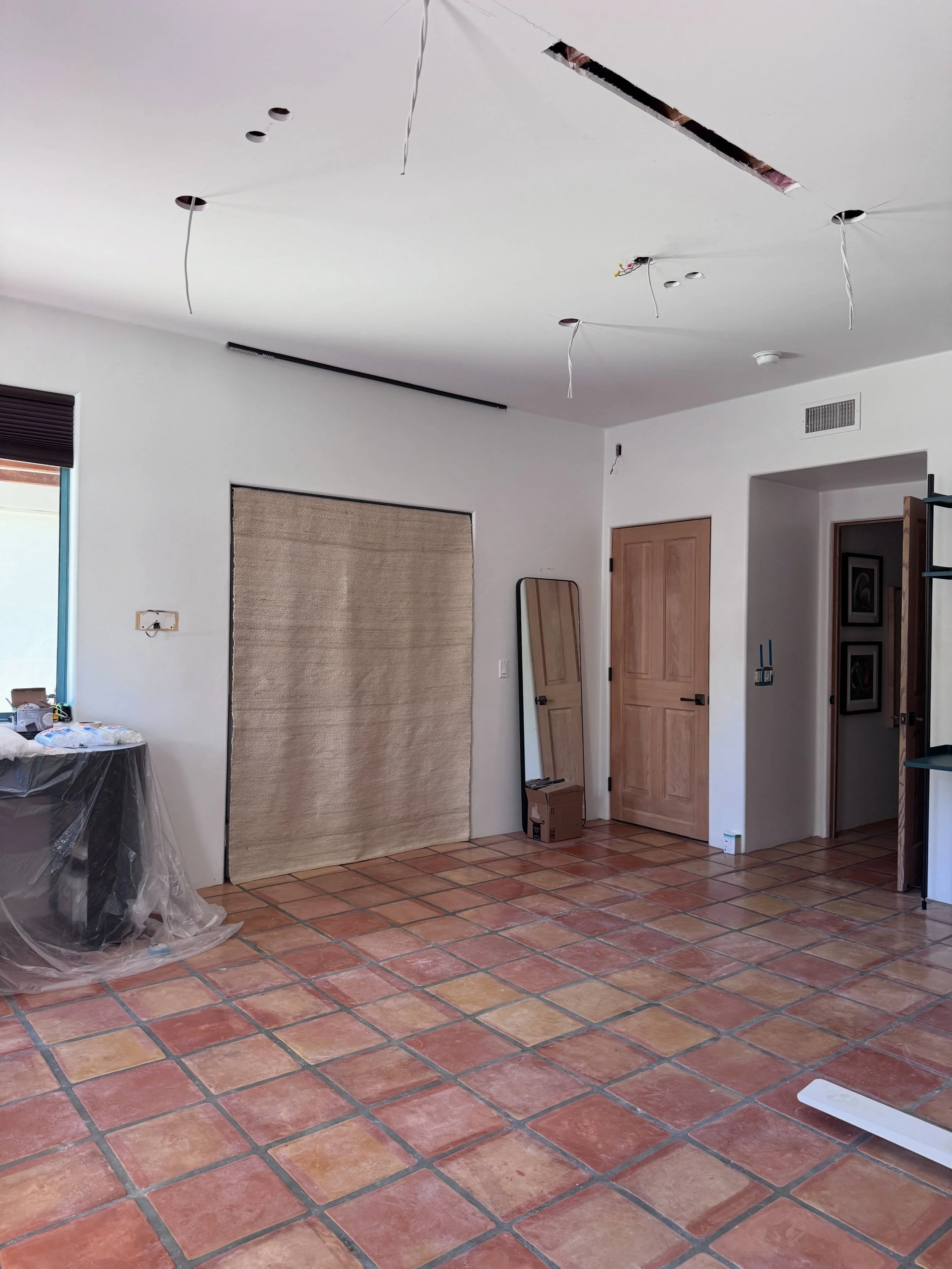 Unfinished interior with exposed terracotta flooring, pale walls, and existing wood doors.