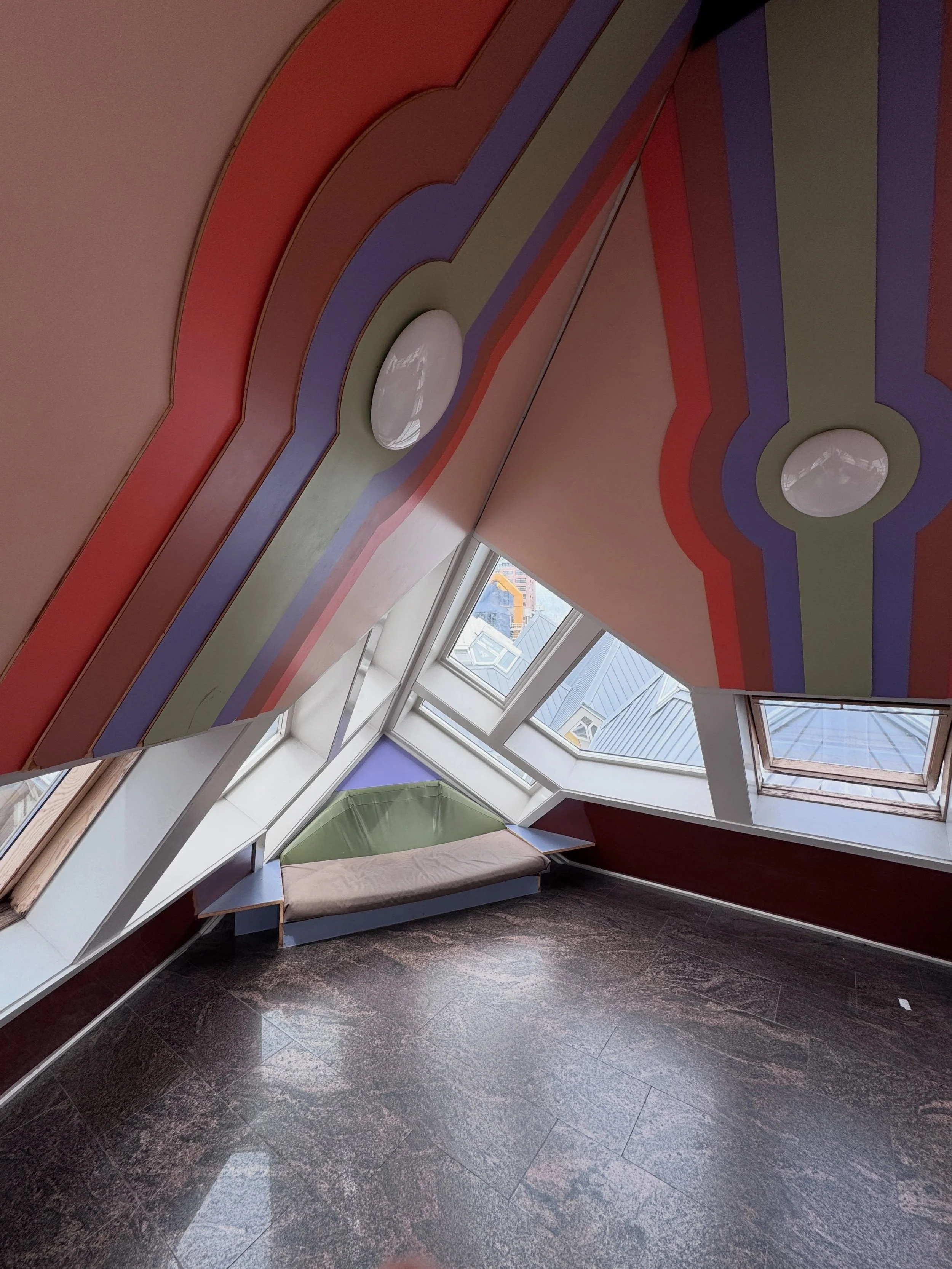 Rotterdam Cube House interior with sloping windows, colorful geometric ceiling bands, and dark stone flooring.