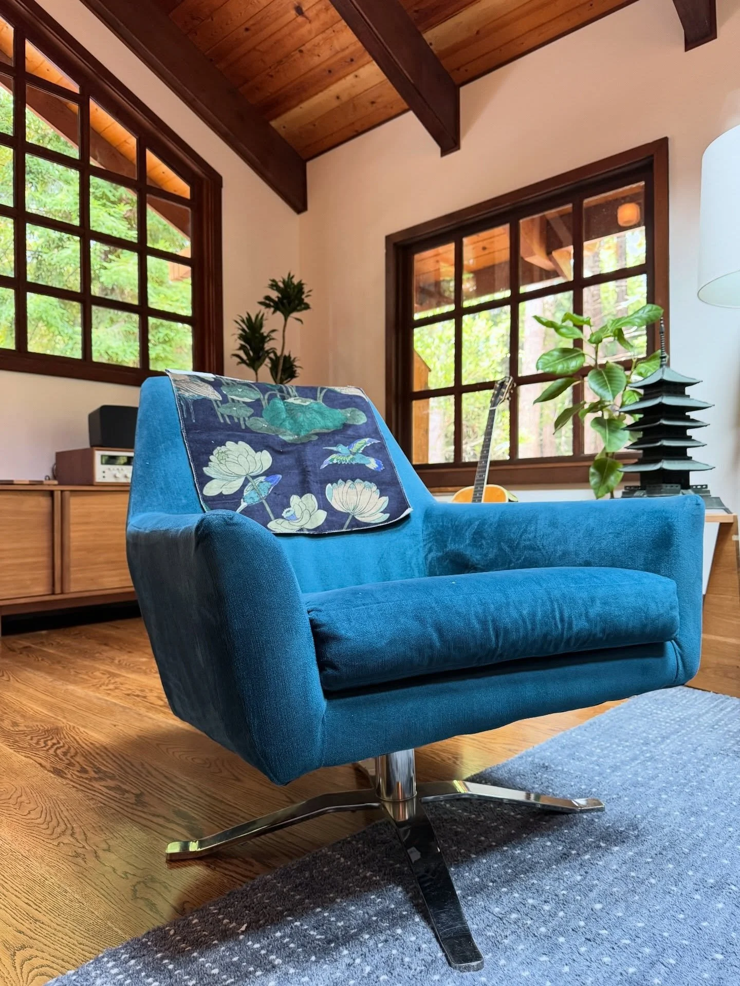 Blue upholstered chair with a botanical cushion beside a vintage rug and wood-framed windows.